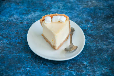 Slice of New York Cheesecake  style with marshmallows on white plate on blue backgroundの写真素材