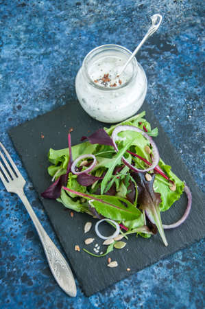 Spring herbs red onion pumpkin flax sesame seeds salad with spicy sour cream sauce served on a black stone board on a blue backgroundの写真素材