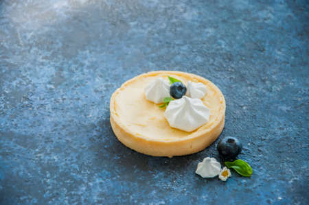 Individual lemon curd tarts with blueberry jam meringue basil leaves on a blue rusty background. Flat lay and copy space.の写真素材