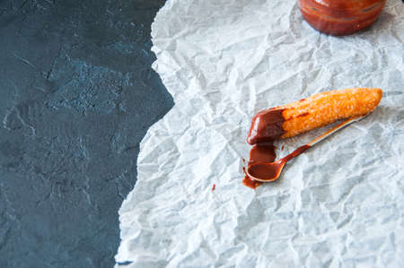 Churros sprinkled with sugar and cinnamon and hot chocolate on a parchment paper on a black stone background. Copy Space.の写真素材