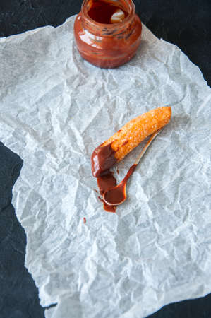 Churros sprinkled with sugar and cinnamon and hot chocolate on a parchment paper on a black stone...