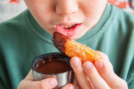 The little boy eating Churros sprinkled with sugar and cinnamon and hot chocolate.の写真素材