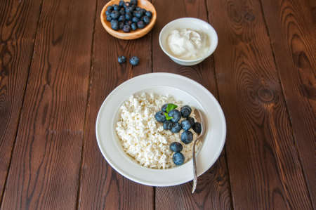 Organic Farming Cottage cheese in a white plate sour cream and blueberries on a wooden background. Copy space.の写真素材