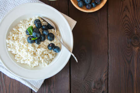 Organic Farming Cottage cheese in a white plate sour cream and blueberries on a wooden background. Copy space.の写真素材