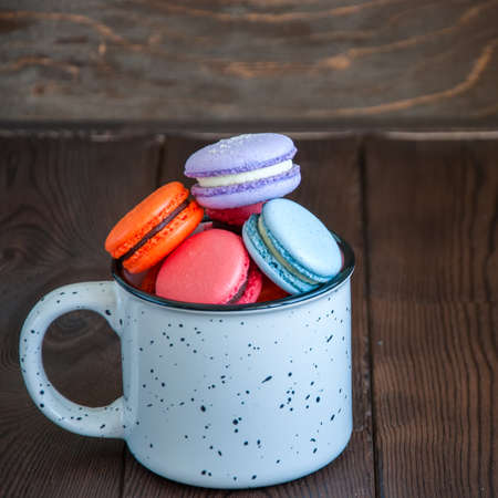 Colorful macarons in a white jar on a wooden background. Close up and copy space.