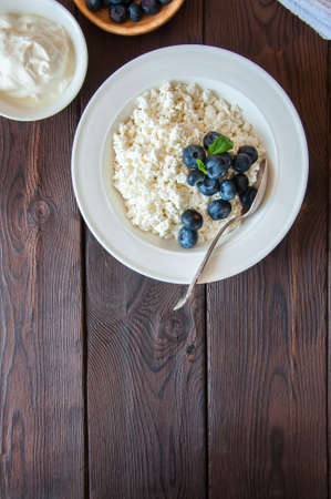 Organic Farming Cottage cheese in a white plate sour cream and blueberries on a wooden background. Copy space.の写真素材
