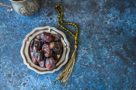Dried date fruits or kurma served on a old vintage palte with ornaments and beads on a blue stone background, ramadan food concept.の写真素材