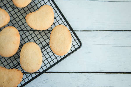 A group of butter shortbread cookies on a wire rack on white wooden background. Selective focus. Close up and copy space.の写真素材