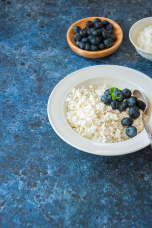 Organic Farming Cottage cheese in a white plate sour cream and blueberries on a blue stone background.の写真素材
