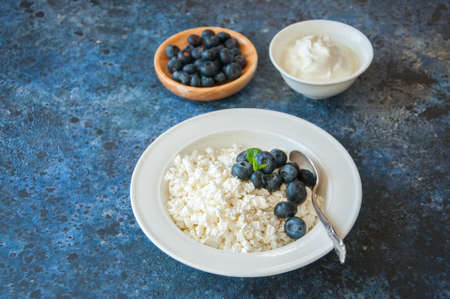 Organic Farming Cottage cheese in a white plate sour cream and blueberries on a blue stone background.の写真素材