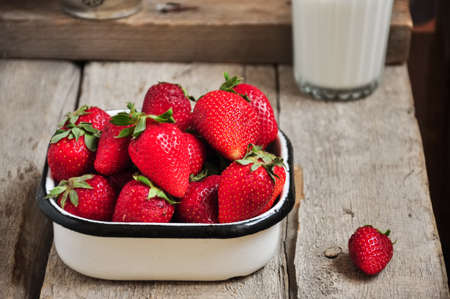 Heap of fresh ripe raw strawberries in a bowl and glass of milk on a wooden background. Rustic style and close up.の写真素材