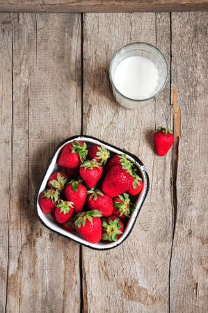 Heap of fresh ripe raw strawberries in a bowl and glass of milk on a wooden background. Rustic style and close up.の写真素材