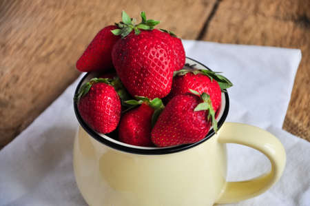 Heap of fresh ripe strawberries with leaves in a jar on a wooden background. Rustic style. Close up.の写真素材