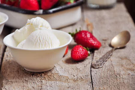 Vanilla ice-cream in a white small bowl with fresh ripe strawberries on a wooden background. Rustic...