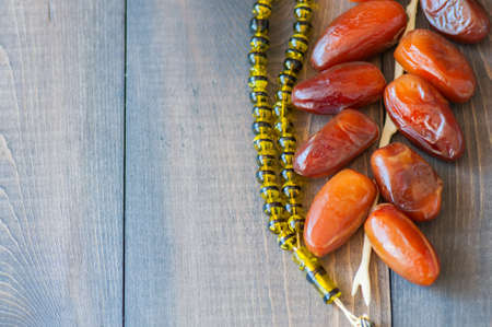 Dried date fruits or kurma and beads on a wooden background, ramadan food concept. Close up. Copy space.の写真素材