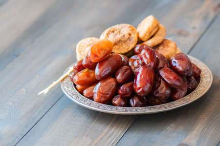 Close up of dried date fruits or kurma and figs served on a old vintage plate with ornaments and beads on a wooden background, ramadan food concept.の写真素材