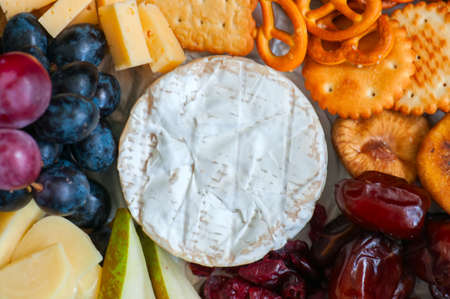 Cheese plate grape salted craker cookies dry dates cranberry, fig, pear pretzels on a wooden board on a black slate background.の写真素材