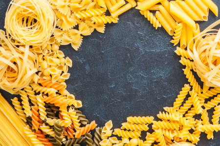Variety of types of Italian pasta background. Set of raw dry pasta on a black slate background.の写真素材