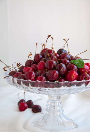 Close up of fresh ripe cherries on a glass cake stand on a white background. の写真素材