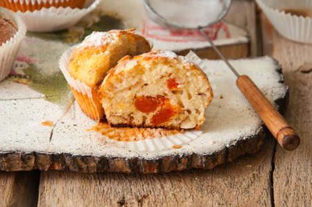 Close up of freshly baked almond and apricot muffins sprinkled with sugar powder and almond petals in a rustic setting on the decorated wooden board.の写真素材
