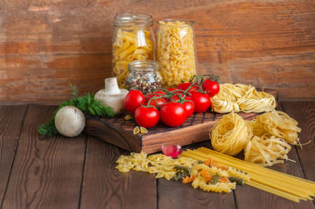 Set of ingredients for italian dinner. Assortment of raw types and shapes of  pasta tomatoes cherry, mushrooms, garlic, spices herbs on a wooden  background. Close up. Top view and copy space.の写真素材