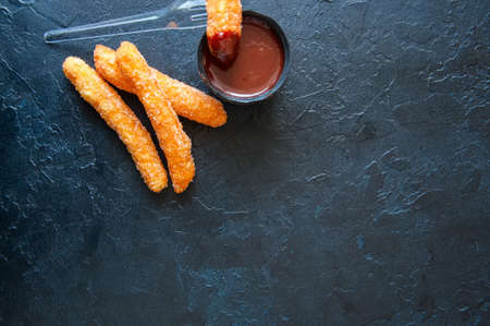 Traditional spanish treat. Popular street food - Churros sprinkled with sugar and cinnamon with hot chocolate sauce in can tin on black slate background. Copy space.の写真素材