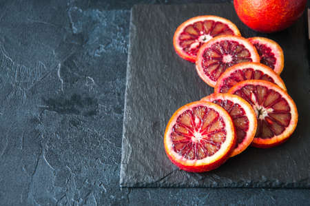 Whole and slices of blood oranges on a black slate background. Copy space and close up.の写真素材