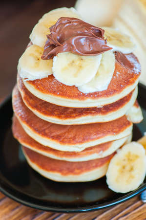 Stack of fluffy panckes with banana and chocolate, blueberry and orange jam served on a plate....