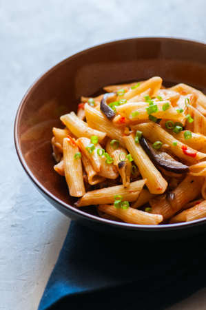 Penne pasta with egplants, tomatoes and green onions on a white stone background.の写真素材