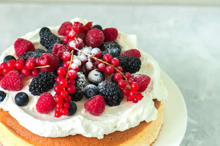 Close up of fluffy Japaniese cheesecake with wipped cream cheese frosting and garnished with forest berries served on a plate over white background.の写真素材