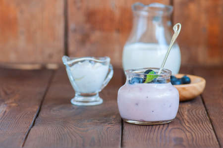 Close up of fresh blueberry yogurt in a jar on a wooden table.