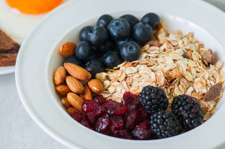 Healthy breakfast concept. Homemade granola (muesli) with blackberry, dry cranberry, blueberry, almond on a white background.の写真素材