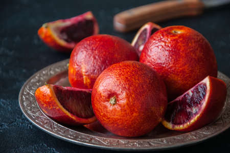 Close up of whole and slices of fresh and ripe blood oranges in a vintage plate on a black slate background. Copy space.の写真素材