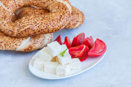 Traditional Turkish bagel (bread) - simit with tomatoes and feta cheese on a plate on a white stone background. Copy space and close up.の写真素材