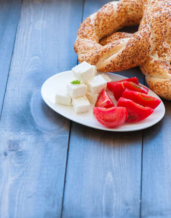 Traditional Turkish bagel (bread) - simit with tomatoes and feta cheese on a plate on a woodenbackground. Copy space and close up.の写真素材