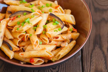 Close up of italian penne pasta with eggplants and tomato sauce in a brown bowl on a white background. Copy space and overhead view. Traditional food concept.の写真素材