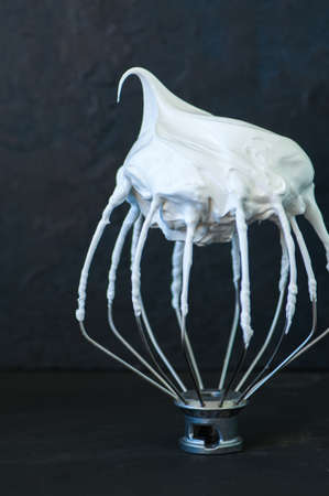 Whipped egg whites - beaten italian merengue on a whisk on black table,  closeup and copy space.の写真素材