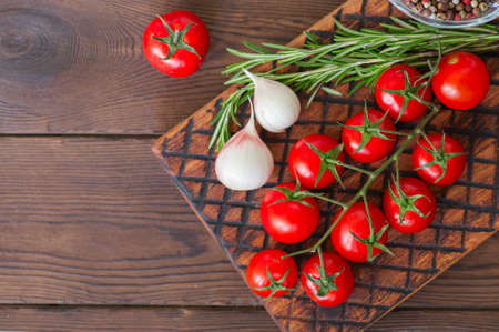Fresh raw cherry tomatoes on a wooden board with pepper garlic and rosemary bunch. Close up and copy space. Top view.の写真素材