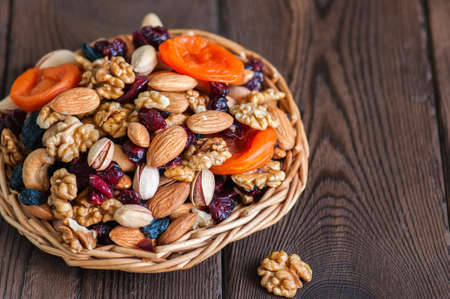 Mix of nuts and dry fruits in a wooden plate. Assortment of walnuts, almonds, roasted cashews, pistachios, dry apricots, cranberries and raisins. Copy space and selective focus.の写真素材