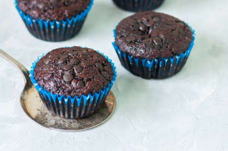 Homemade rich double chocolate muffins with chocolate chips on a wire rack on a white stone background. Close up and copy space.の写真素材