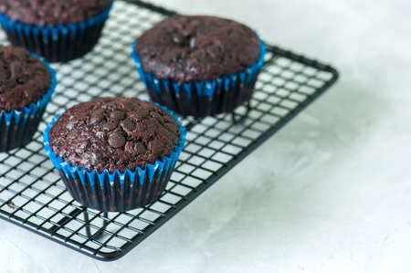 Homemade rich double chocolate muffins with chocolate chips on a wire rack on a white stone background. Close up and copy space.の写真素材