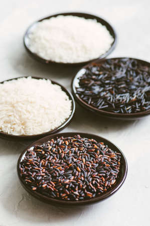 Set of various rice in plates on white stone background: black, basmati, brown and jasmine rice. Toned.の写真素材