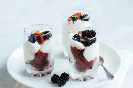 Red velvet sponge cake with cream cheese decorated with fresh berries - dessert in a glass. White stone background.の写真素材