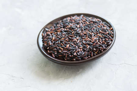 Brown rice in a plate on white stone background. Toned.の写真素材