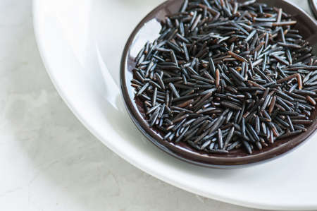 Black rice in a plate on white stone background. Toned.の写真素材