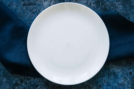 Empty white round plate and linen blue sackcloth on a stone background.の写真素材