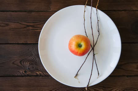 White plate, red apple and tree brunches on a wooden background. Autumn, Thanksgiving, Halloween concept.の写真素材