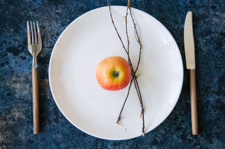 White plate, red apple, cutlery and tree brunches on a blue stone background. Autumn, Thanksgiving, Halloween concept.の写真素材