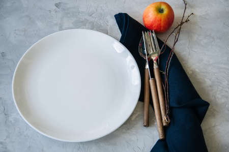 White round plate, red apple and  tree brunches on a wooden background. Autumn holidays concept.の写真素材