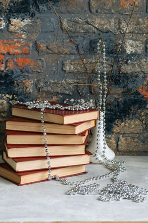 Stack of old books, branches in vase with garland, brick backgroundの写真素材